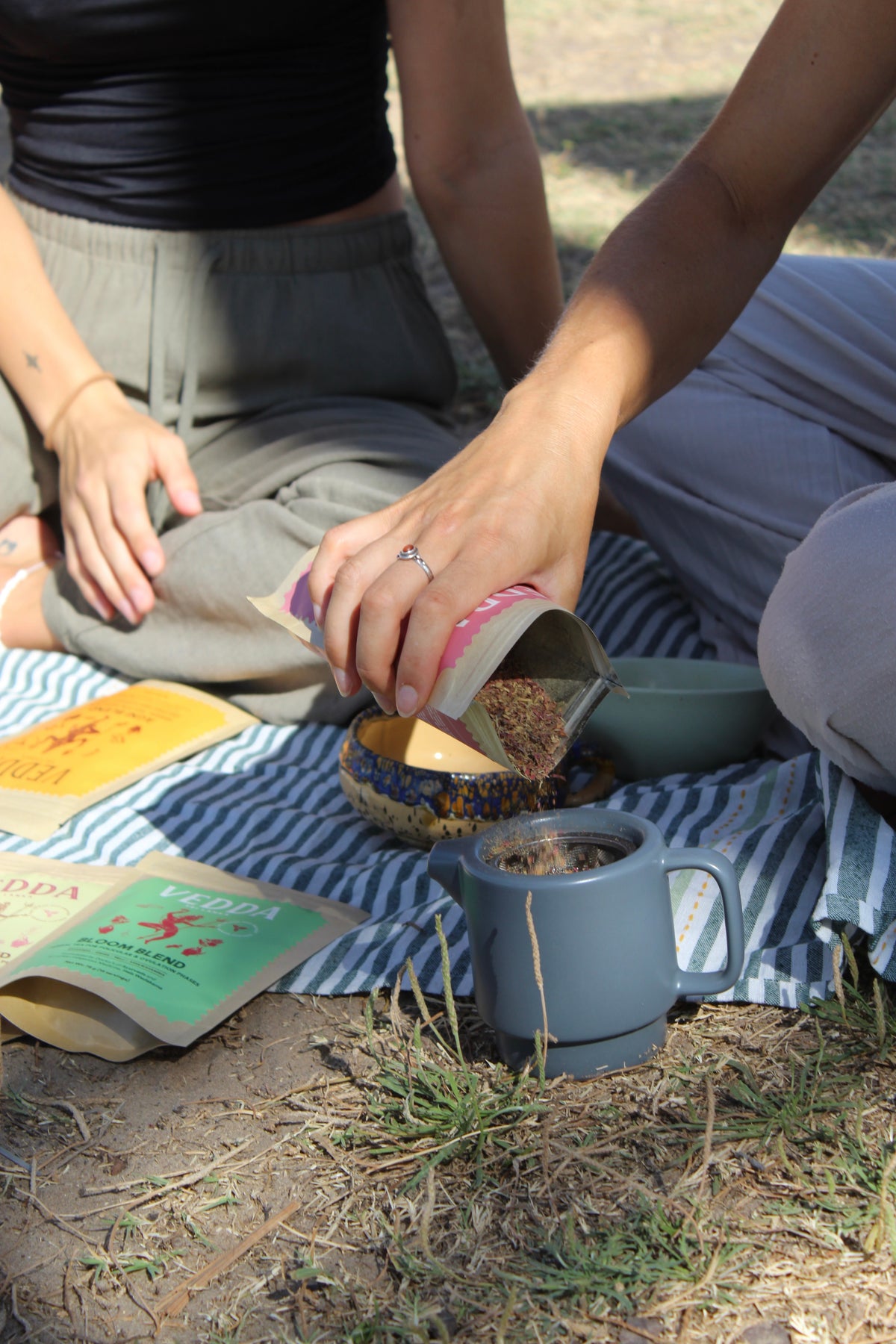 Hands pouring tea into small cups on a picnic blanket
